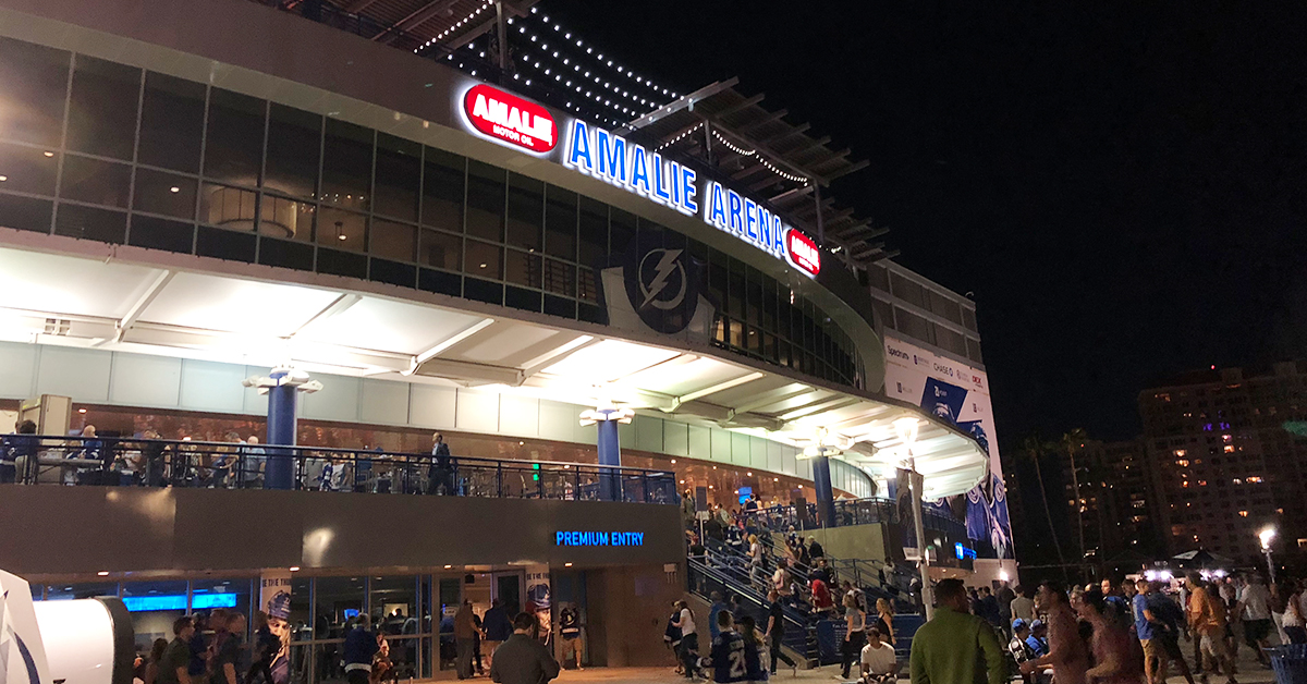 Exterior of a hockey arena at night with fans proceeding inside