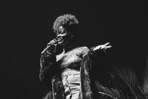 A black and white photo of Ari Lennox singing into a microphone