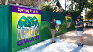 A sign for Iron Gwazi on a green construction fence in front of the rollercoaster under construction