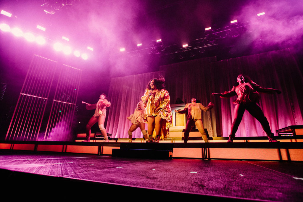 Lizzo performs on stage surrounded by four backup dancers.