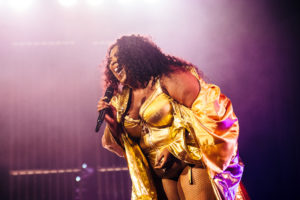 Lizzo sings into a microphone while wearing a shiny gold bodysuit