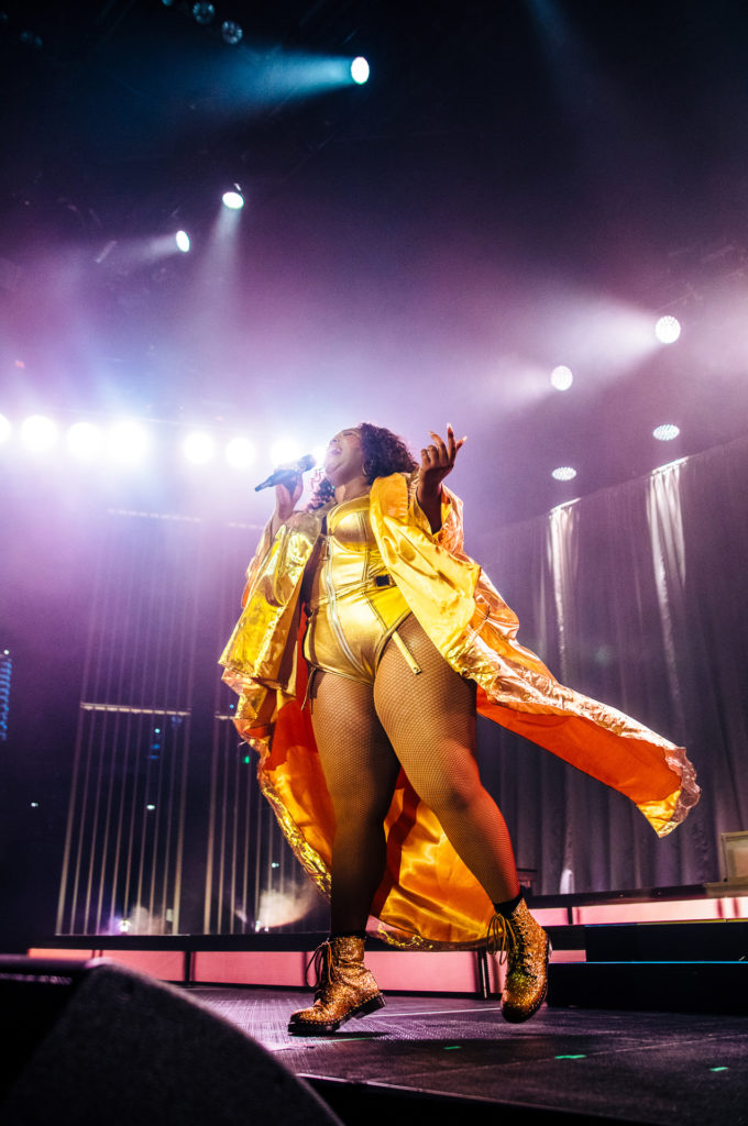Lizzo sings into a microphone with one foot slightly off the ground