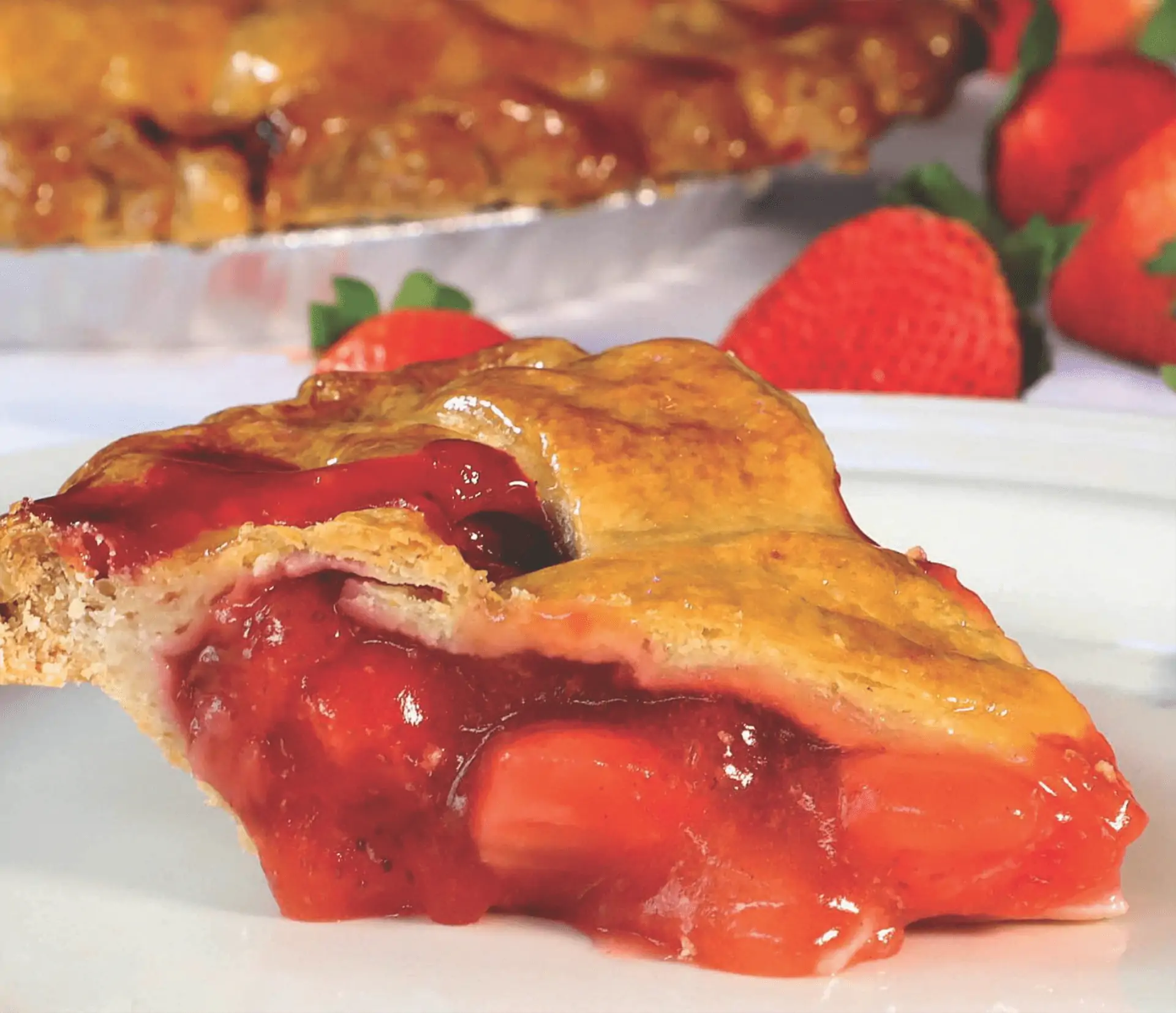 Slice of cherry pie with various whole fruits visible in the background. 