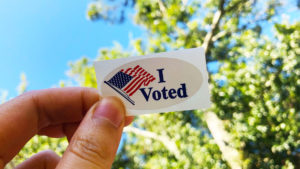 I voted sticker held up against blue sky and tree
