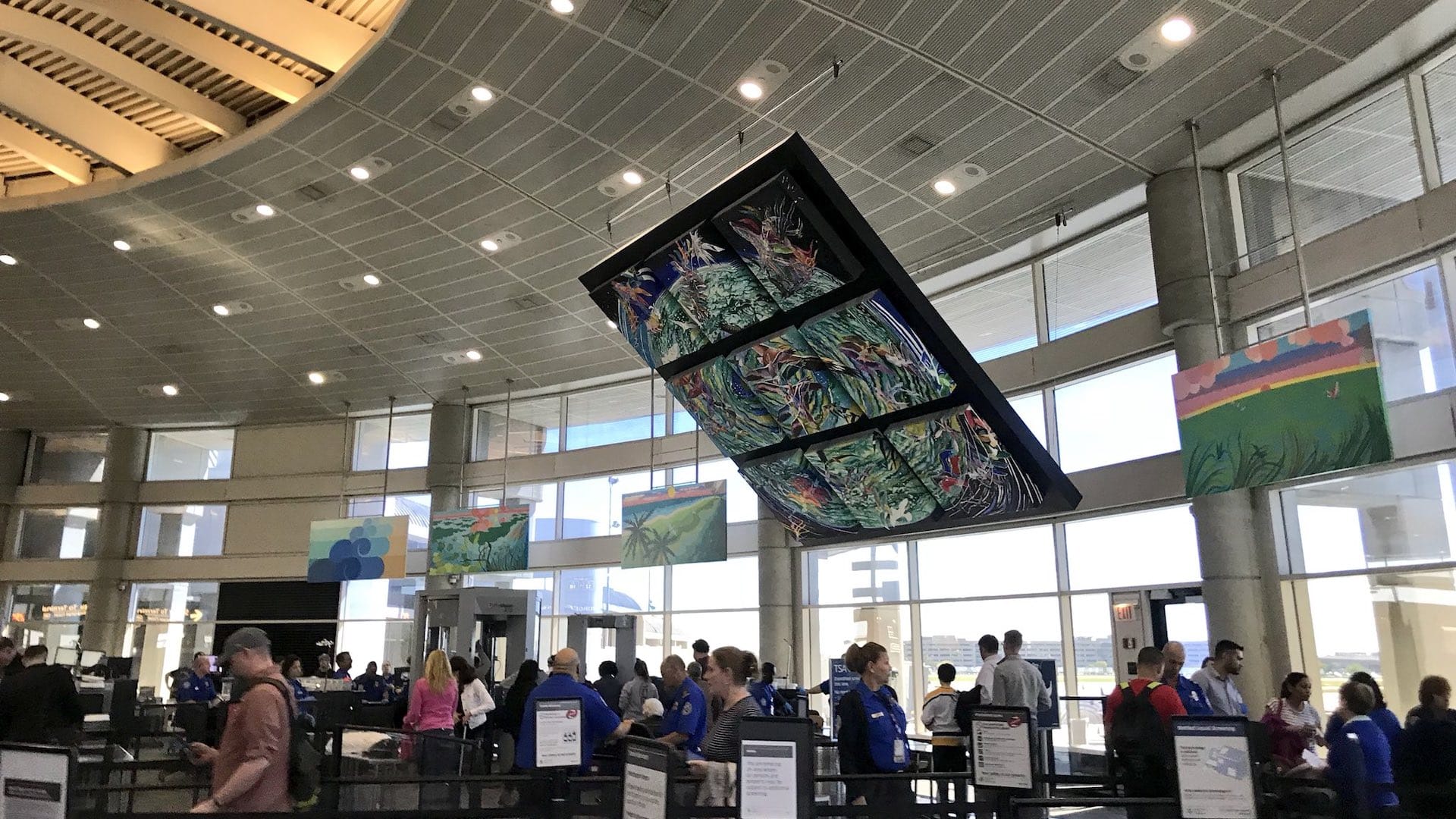 A large mosaic is positioned from the rafters as airport passengers pass through a terminal