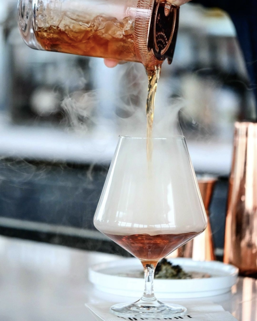 Dark liquor being poured into a smoking cocktail glass. 