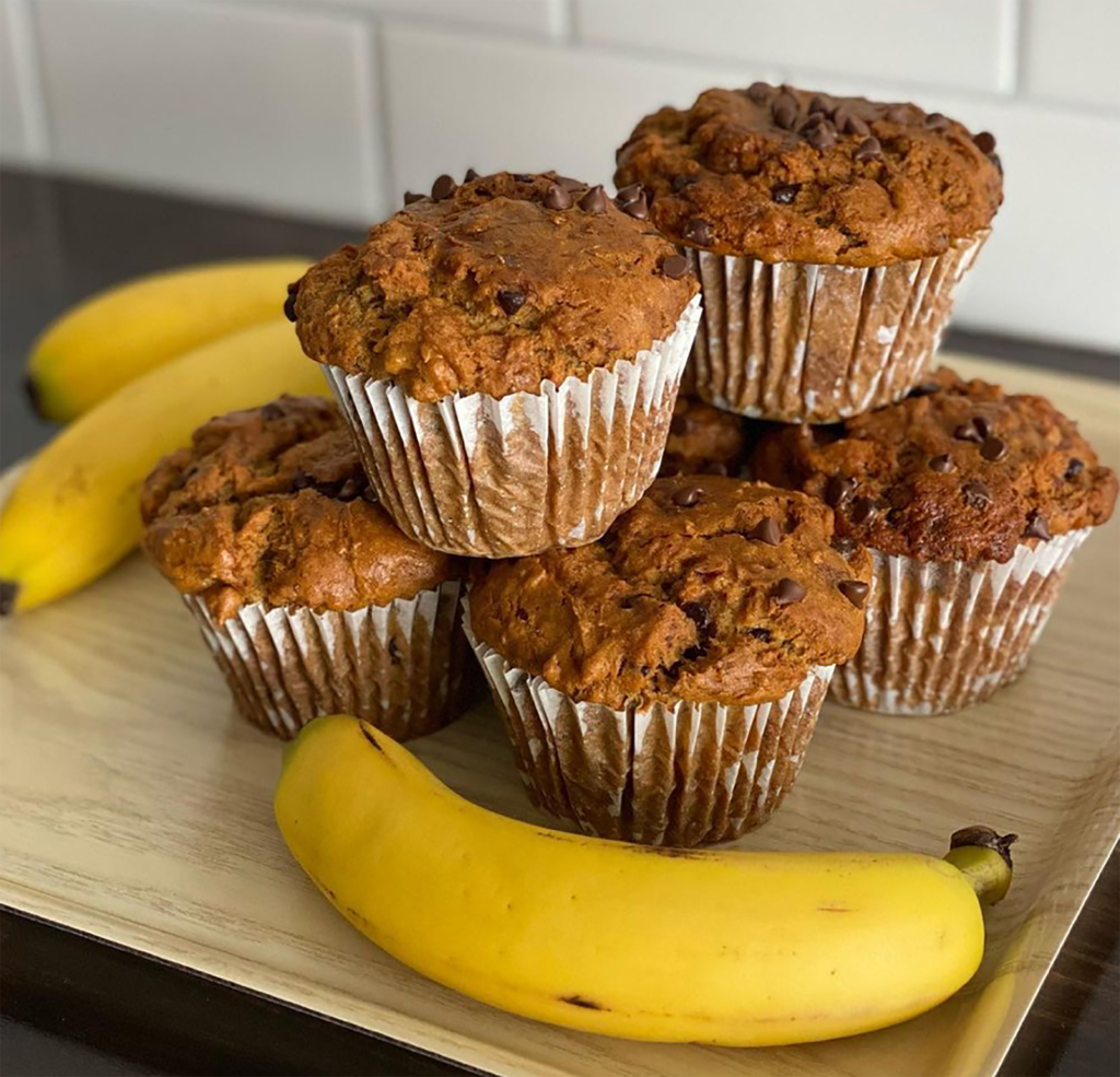 fresh muffins stacked on top of one another surrounded by bananas