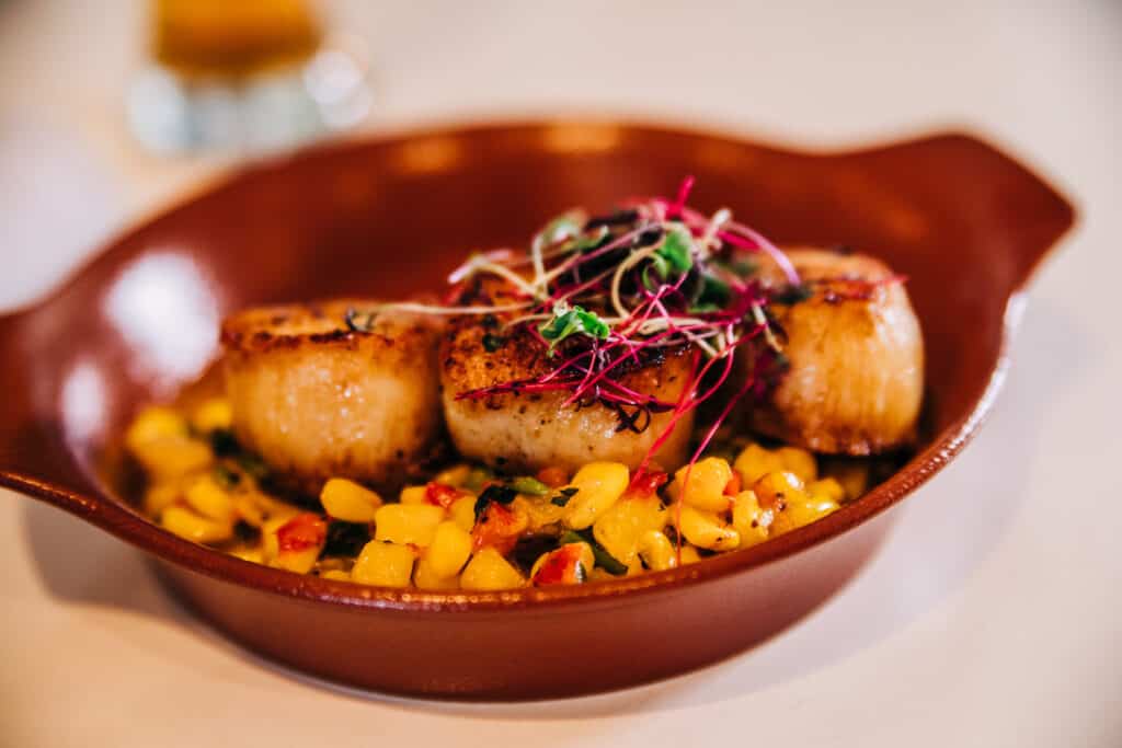 seared sea scallops with sprouts on top and yellow corn. 