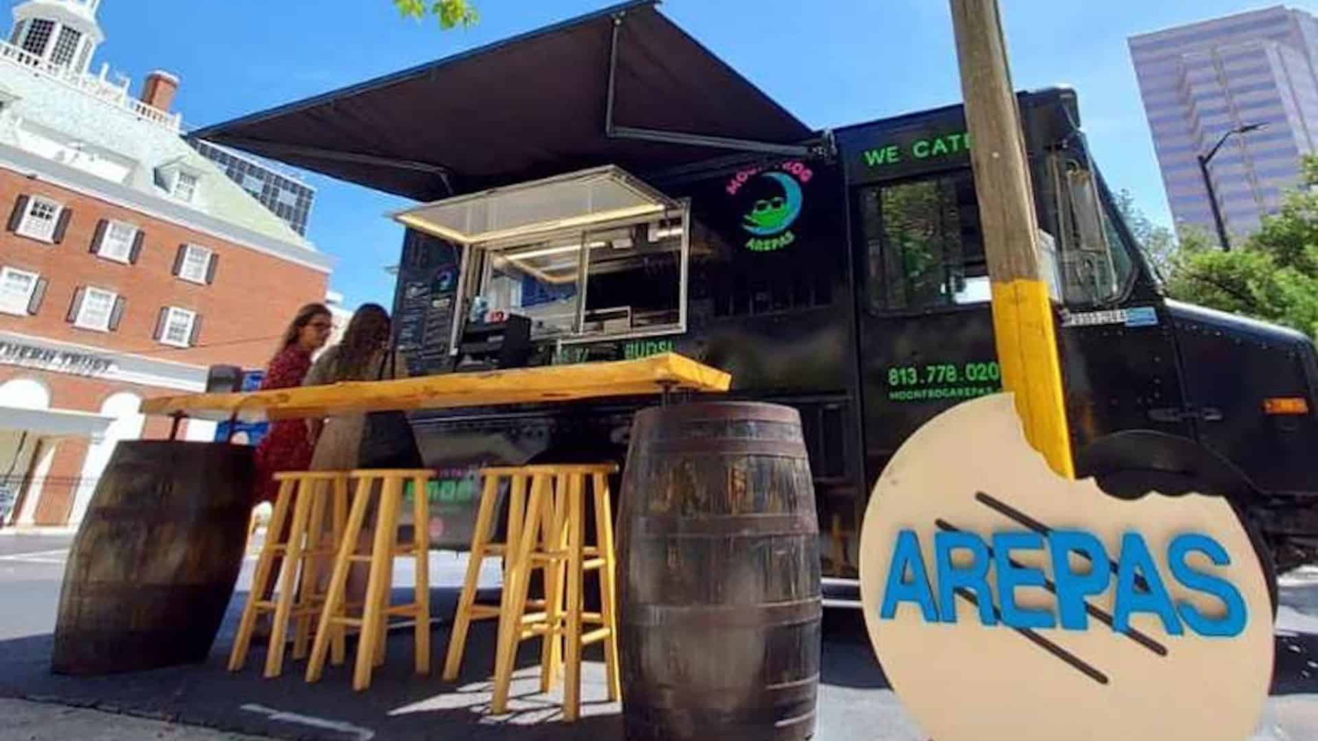exterior of a food truck with a black wrap and a wooden high top table set on the sidewalk