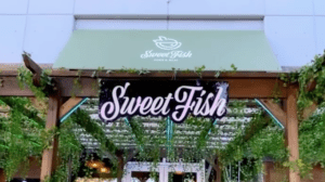 exterior of a restaurant with green vines hanging from a wooden archway and a purple sign reading sweetfish above the entrance