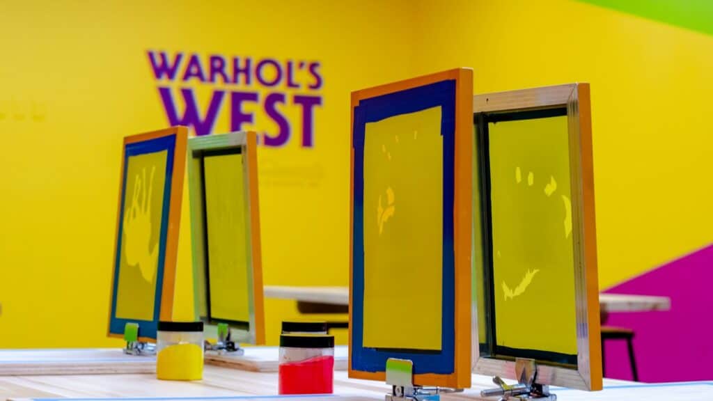 A variety of silk screen machines in a room with bright yellow walls and purple lettering on the back