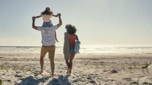 a couple walking on the beach with child on their shoulders