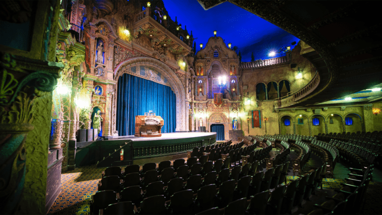 inside an old theatre with a blue velvet curtain on stage and a pianist at the center