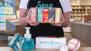An employee in an apron holds a box of soap with 5 different color bars inside