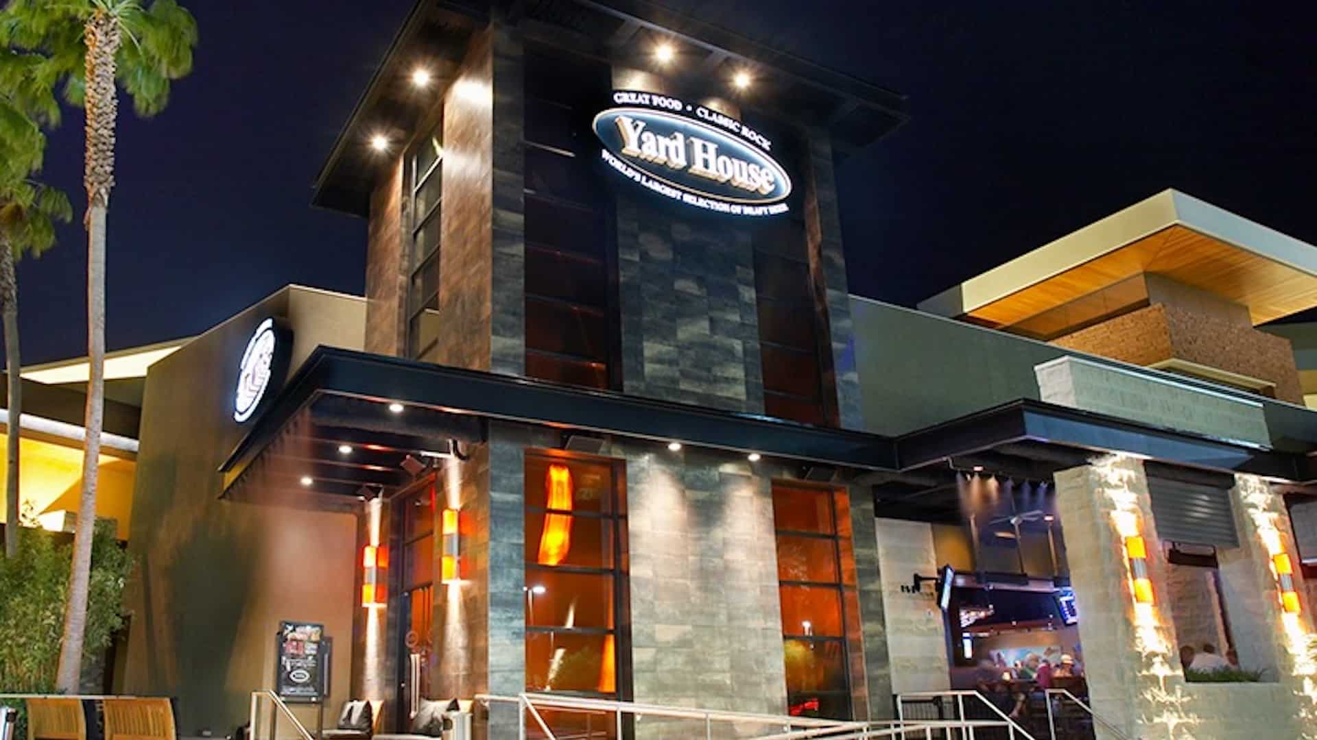 Exterior of a restaurant with stone walls, and lit up sign that reads "Yard House"