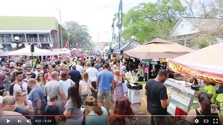 A group of people gathered for a food festival in a downtown area. Multiple tents are set up along a city block.