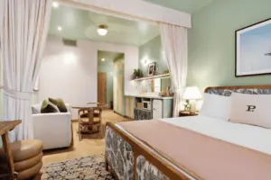 interior of a boutique hotel room with pink linen curtains, and pink bed sheets. The room has green walls and a beach painting over the bed.