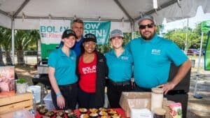 5 people in blue shirts smiling at camera in food tent