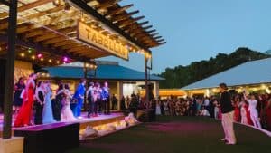 A large outdoor stage covered in string lights with multiple people in suits and dresses under an awning