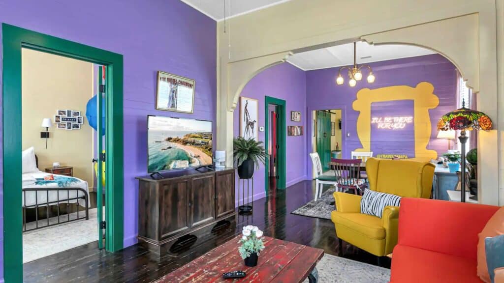 Inside an apartment with purple walls, and a giant gold frame around a neon sign