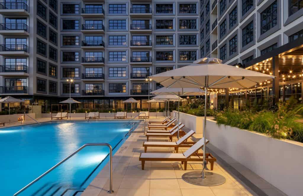 Rooftop pool deck at night. Lounge chairs surround the pool. Balconies tower over the pool. 