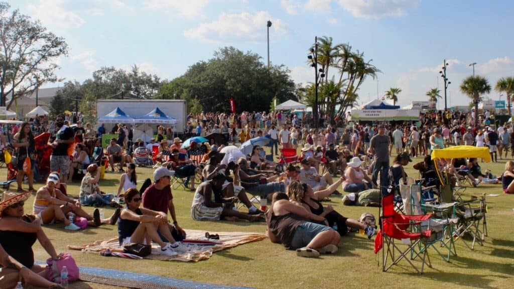 A large outdoor riverfront park with people laying on. blankets next to vendor tents