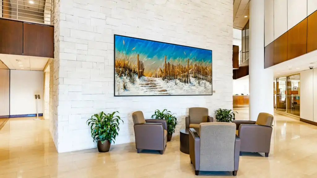 inside an office building. a large painting hangs from a marble wall. 4 leather chairs are arranged around a small coffee table