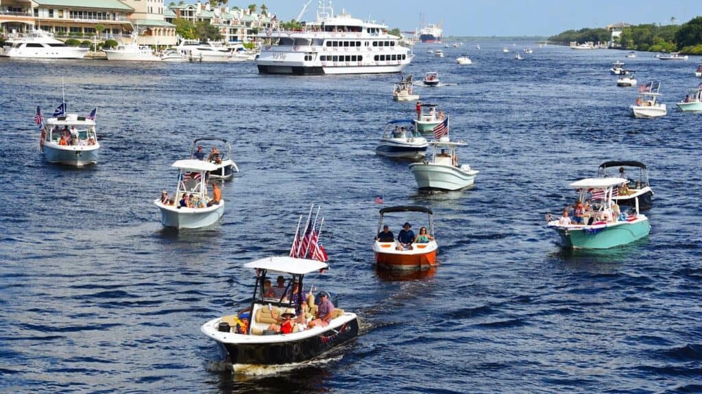 a procession of boats moving down river from a populous waterfront neighborhood. a cruise ship is seen in the background