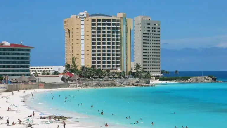 photo of a beach with two tall hotels seen in the background. The water is crystal.