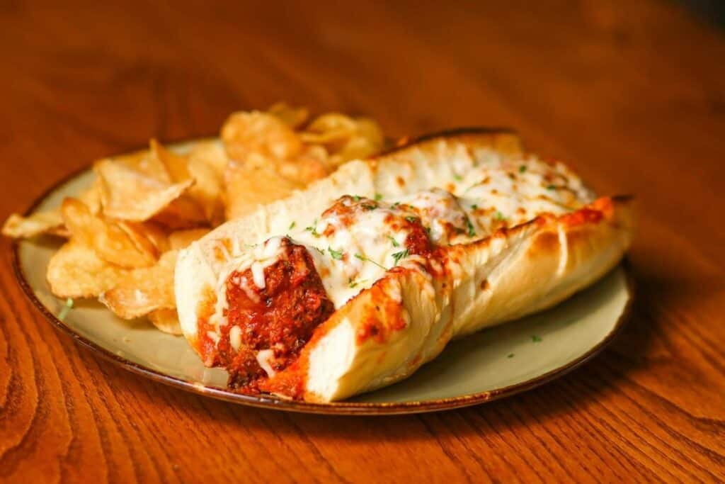 a meatball sub with cheese melted on top plated next to a generous portion of potato chips