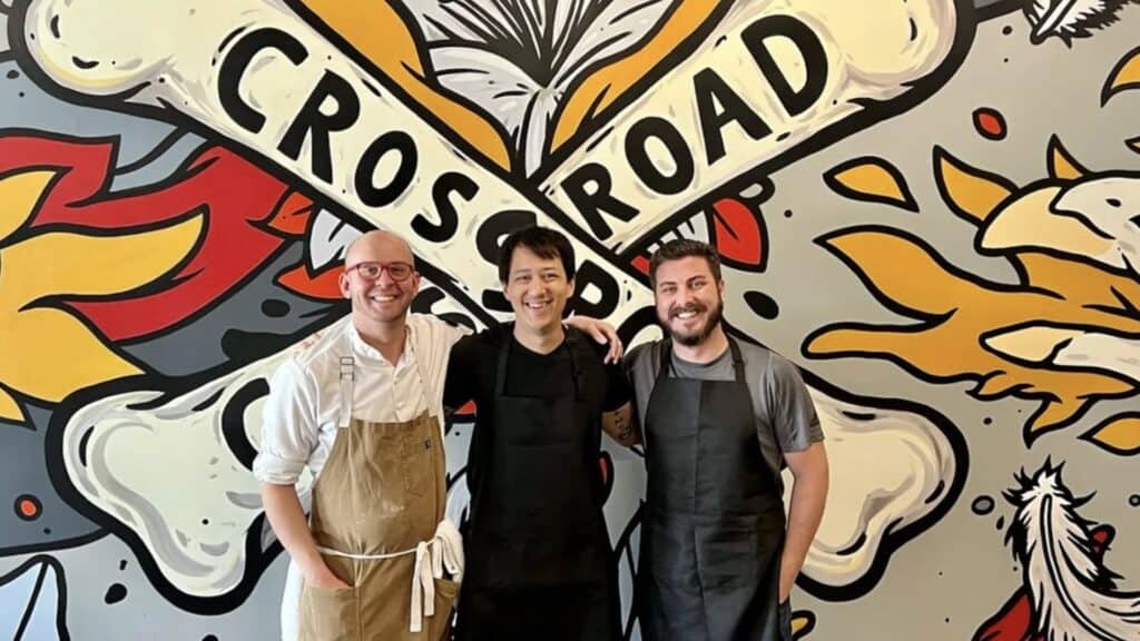 three people in chef's aprons stand in front of a mural featuring a skull and crossbones