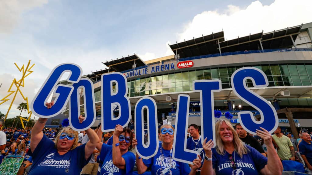 Outside a sports stadium. fans hold up giant blue letters that spell GO BOLTS