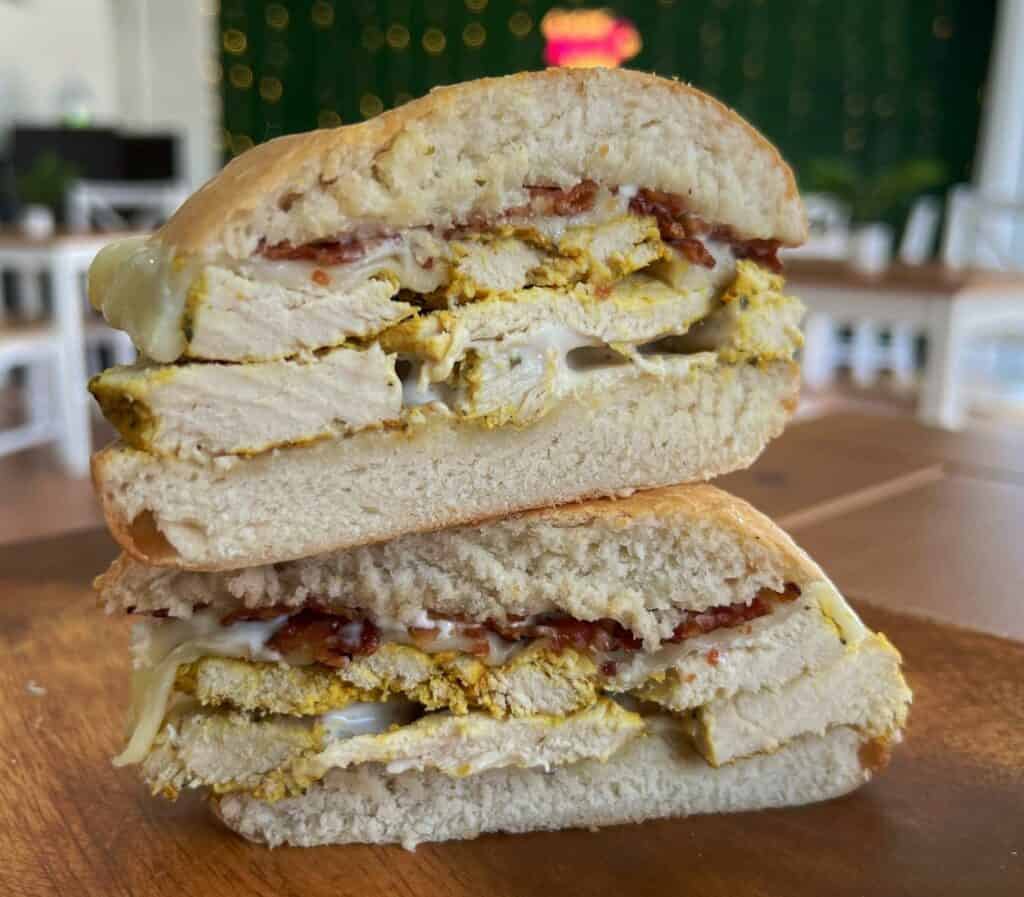 Stacked chicken sandwich with yellow mustard sauce and bacon sticking out from the cut hard roll.