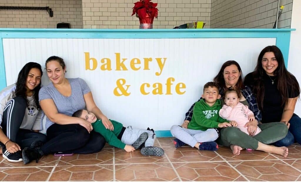 a family sitting in front of a white counter with the words bakery and cafe painted in yellow on the front.