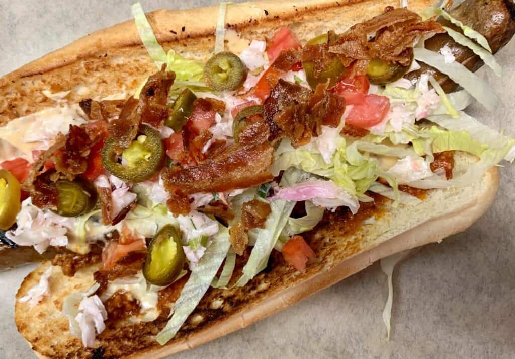 a super long hot dog topped with peppers, lettuce, and sauce. 