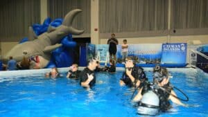 A group of people in scuba suits dive in a pool in an indoor arena