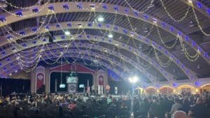 inside a convention center with lights hanging from the ceiling, and a wrestling ring set up at the center