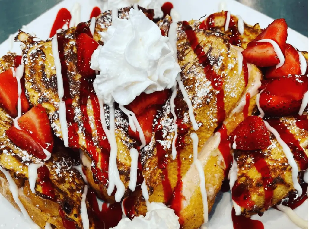 A plate of French Toast covered in chocolate sauce, whipped cream, and strawberries. 