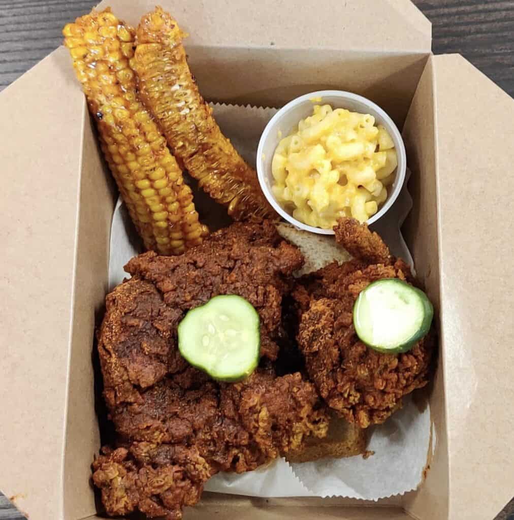 plate of fried chicken and a cup of Mac and cheese next to two fried corn cobs