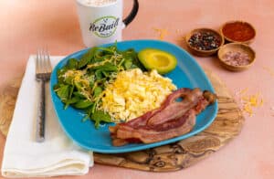 Bacon, eggs, avocado, and greens on a bright blue plate
