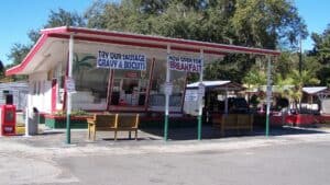 Exterior of a roadside farm stand with signs for breakfast and lunch hanging from the exterior