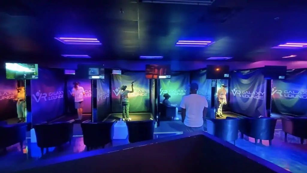 A collection of gamers stand in individual VR booths and game under purple lights.