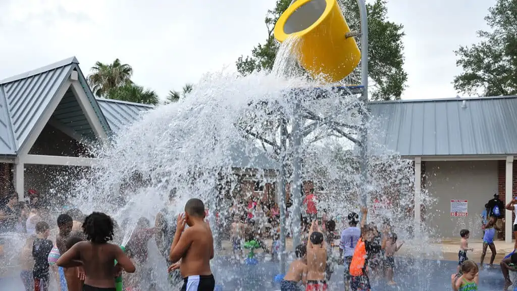 A large yellow bucket pours gallons and gallons of water on guests at an outdoor park.