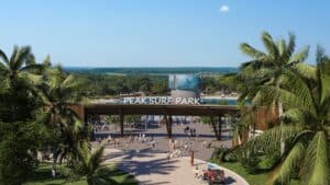 rendering of a surf park entrance. Trees frame the entrance. A large pool can be seen in the distance.