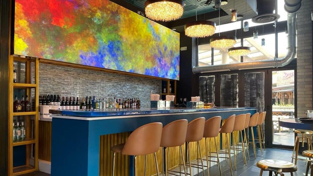 A bar with a vibrant rainbow mural on the wall above the shelves of liquors.