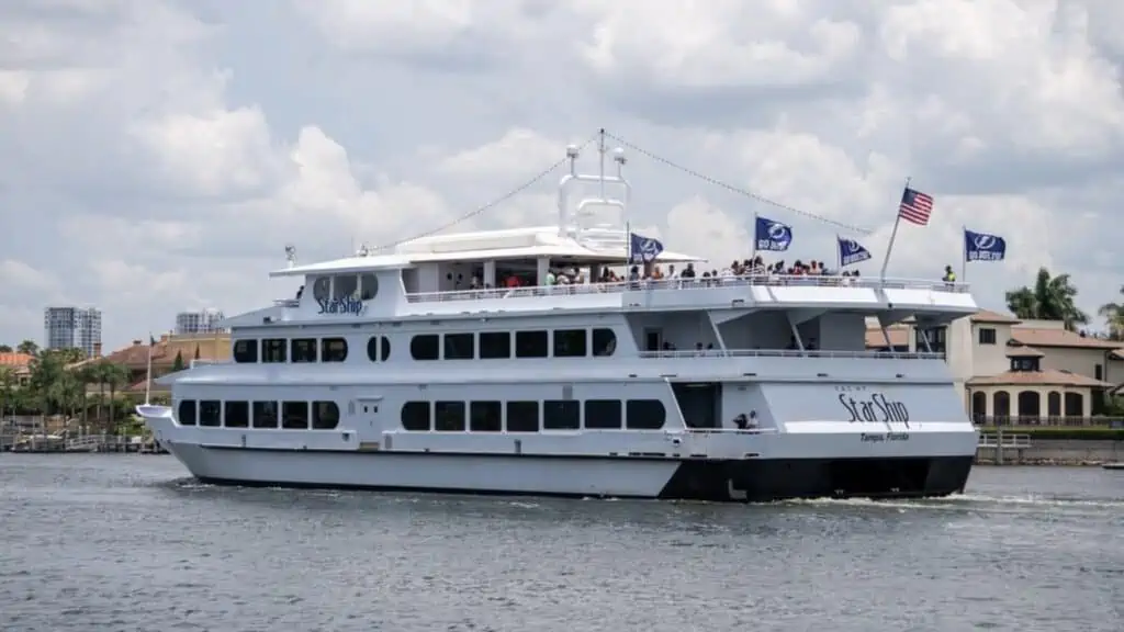A large vessel spanning three floors floats in the water. Multiple blue NHL flags are set on the back of the boat. 