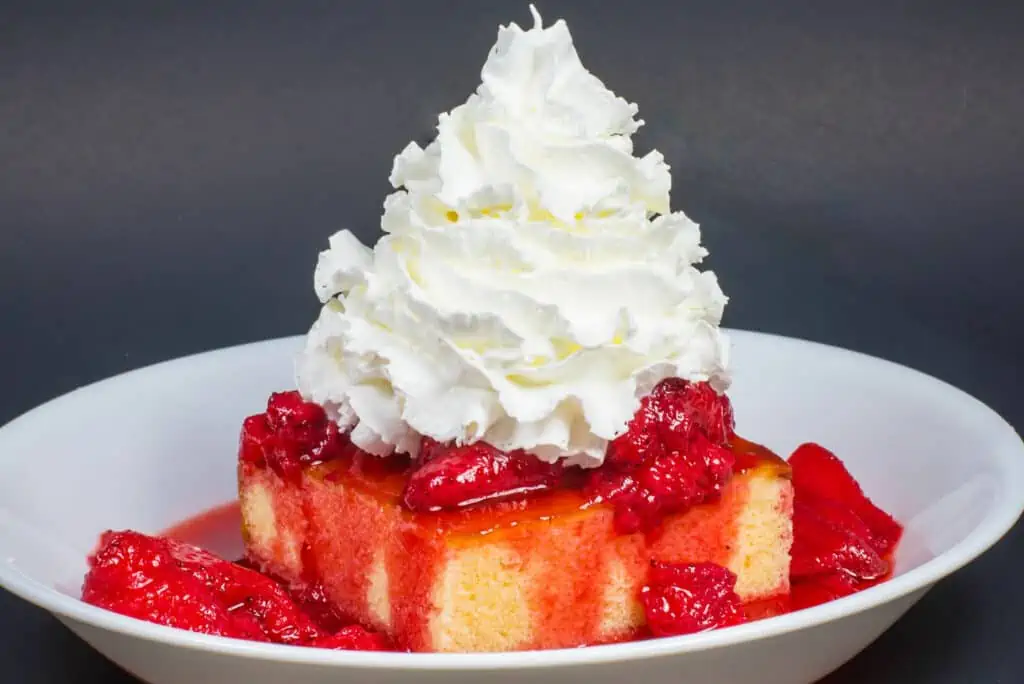a strawberry shortcake topped with whipped cream and fresh strawberries sliced on top