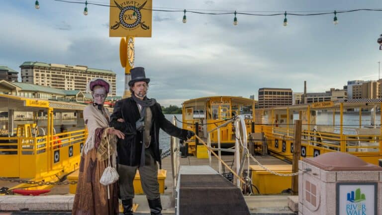 Two ghostly figures stand in front of a dock for large yellow water taxis.