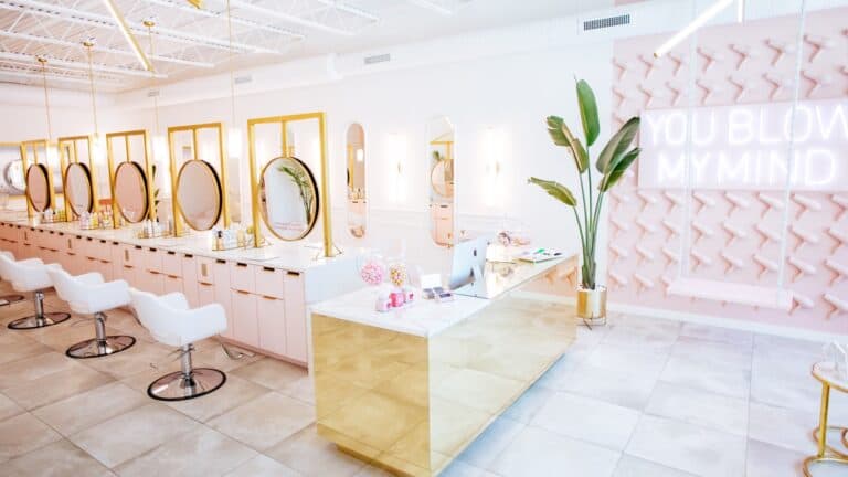 inside a light pink blow dry bar with multiple salon chairs set up next to mirrors