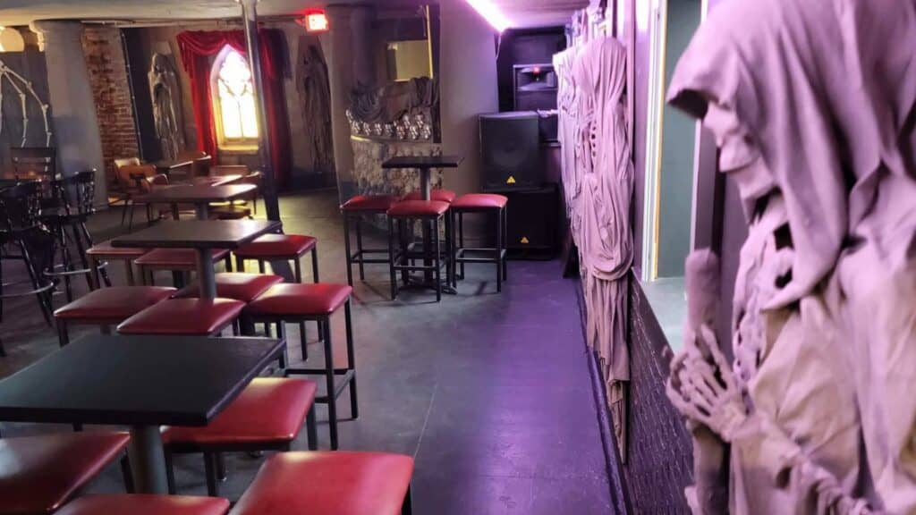 Interior of a cocktail bar with a large skeleton draped in white fabric situated at the front of the bar. Spooky decor surrounds the seating